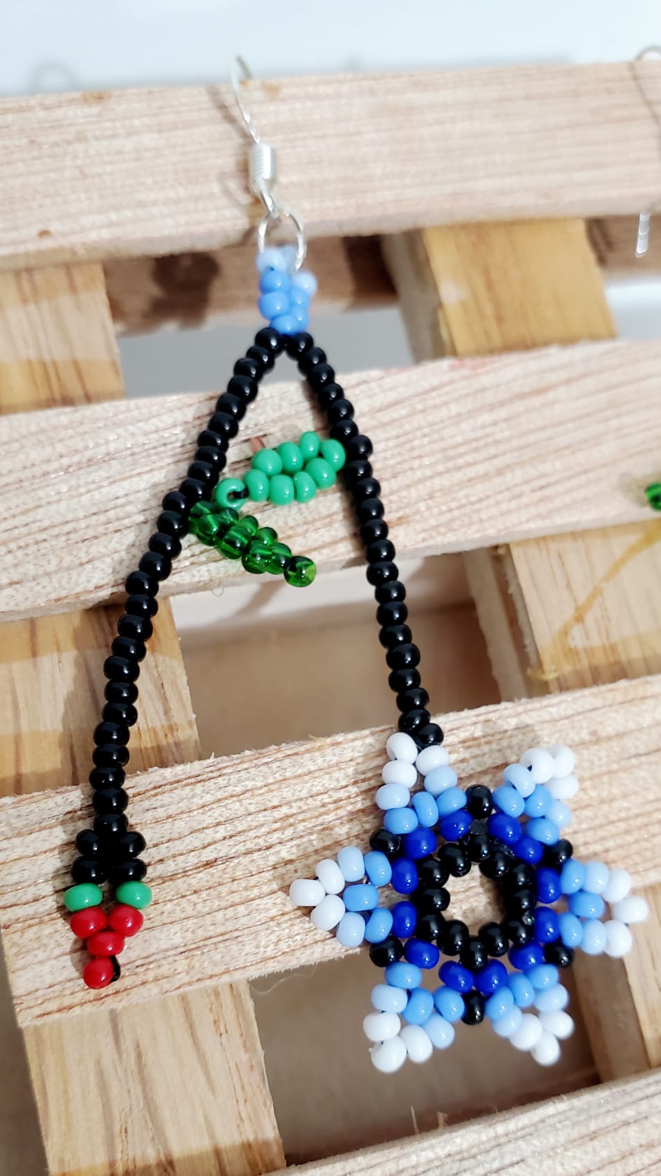 Single beaded earrings long with black beads, with two chains, blue and white flower at one end and small cherry with petals on the other. Earring has hook metal.